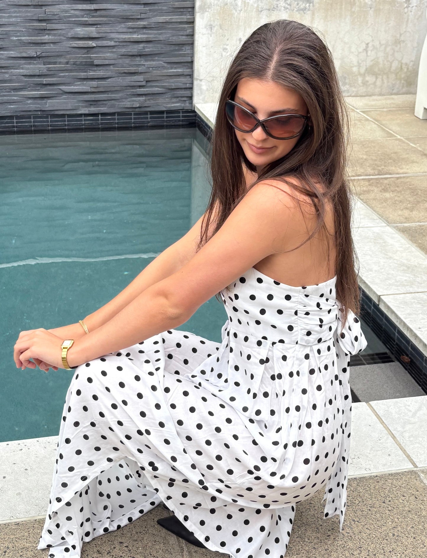 Woman in a polka dot dress sitting by a poolside.