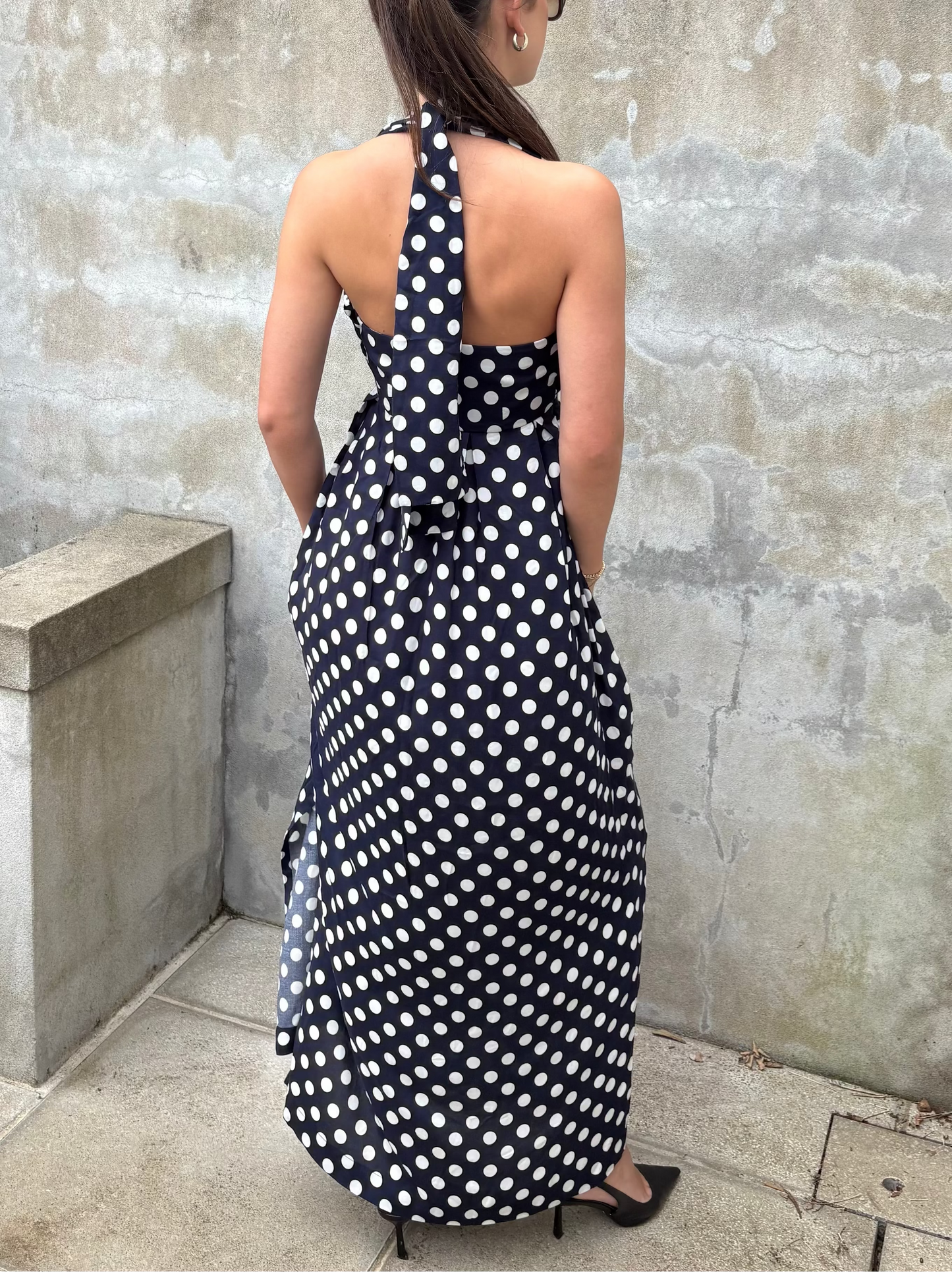 Woman wearing a navy and white polka dot maxi dress against a textured wall.
