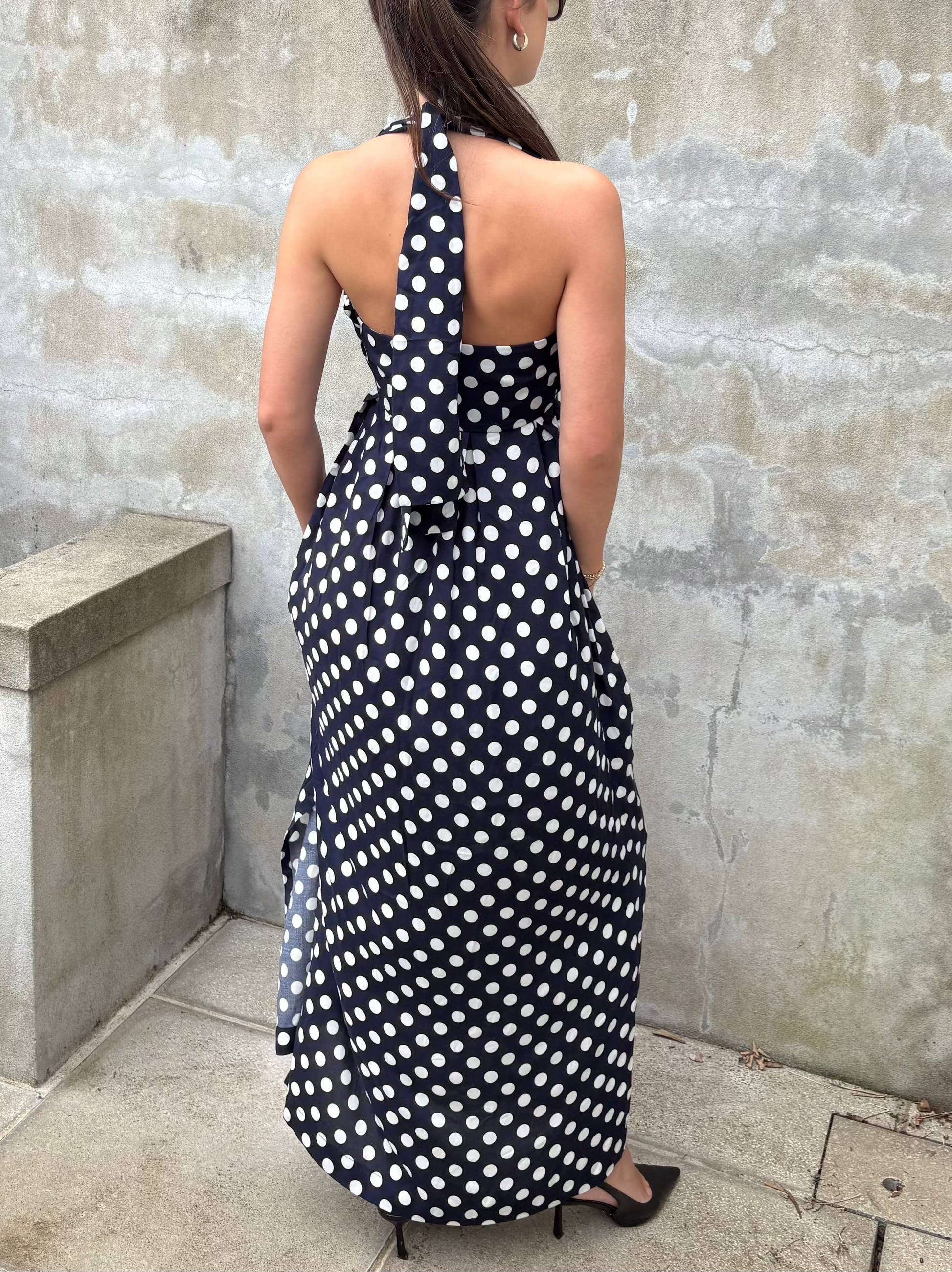 Woman wearing a navy and white polka dot maxi dress against a textured wall.
